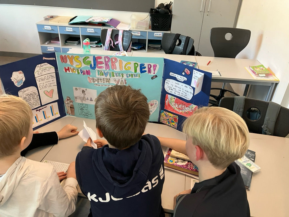 En gruppe barner som sitter ved et bord med en plakat