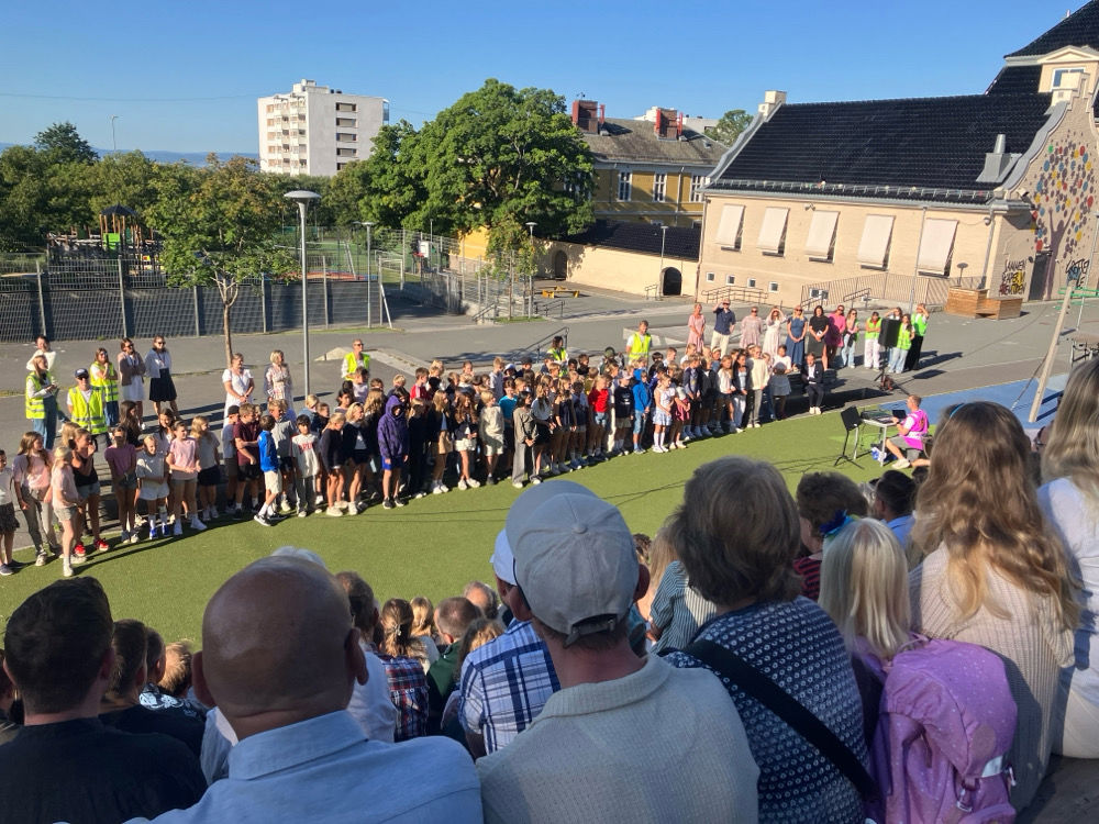 En gruppe mennesker som står i en skolegård med en folkemengde som ser på